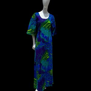 Può includere: Un abito lungo e fluido con un vivace motivo floreale nelle tonalità del blu, verde e viola. L'abito presenta uno scollo tondo e maniche corte. L'abito è esposto su un manichino su sfondo nero.