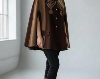 May include: A brown cape with a decorative floral design and a matching hat. The cape has a pocket and button closure. The outfit is paired with black trousers and brown cowboy boots.