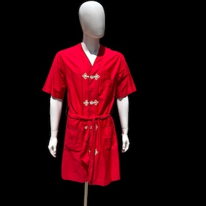 May include: A red short-sleeved robe with white frog closures and a matching belt. The robe has two front pockets and is displayed on a mannequin against a black background. The robe is a solid color.