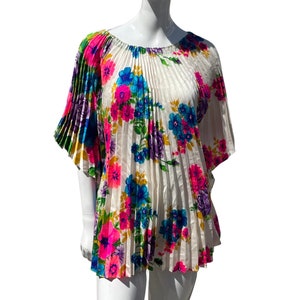 May include: A white, pleated blouse with a floral print in shades of pink, blue, yellow, and purple. The blouse has a scoop neck and short sleeves.