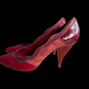 May include: A pair of red high-heeled shoes with a snakeskin pattern. The shoes have a pointed toe and a stiletto heel.