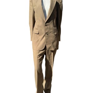 Puede incluir: Un traje beige con una chaqueta de un solo botón y pantalones a juego. La chaqueta tiene solapa de muesca y cierre de dos botones. Los pantalones tienen pierna recta.