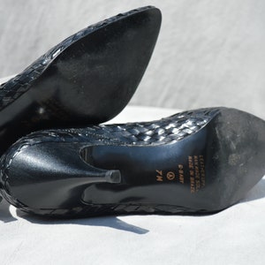 Pu&ograve; includere: Scarpe con tacco in pelle nera intrecciata con punta a punta. Le scarpe hanno un'etichetta di misura 7M sulla suola e riportano "Leather Upper, Man Made Sole, Made in Brazil, C-Balt" sul fondo.