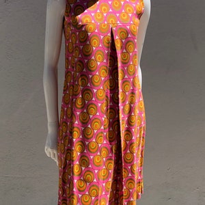 Puede incluir: Un vestido rosa sin mangas con cuello blanco y un patrón geométrico de círculos naranjas y verdes.