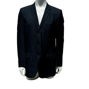 May include: A dark navy blue blazer with a three-button closure, notched lapels, and two front pockets. The blazer is displayed on a white mannequin. The jacket has a classic, tailored fit.