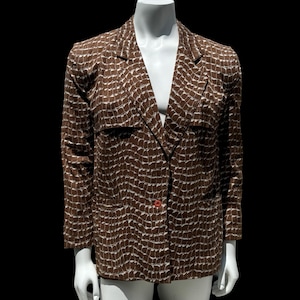 May include: Brown blazer with a white pattern, displayed on a mannequin. The blazer has a single red button closure and two front pockets. The pattern is a repeating geometric design. The blazer is a classic style.