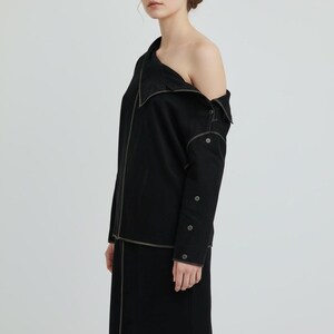 May include: A black two-piece outfit featuring a long-sleeved top with an off-the-shoulder design and a knee-length skirt. The outfit has light-colored stitching and button details. The model is wearing the outfit.