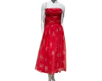 Puede incluir: Un vestido rojo sin tirantes con estampado floral. El vestido está hecho de una tela transparente y tiene un corpiño ajustado y una falda fluida.