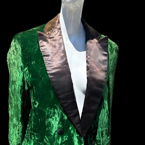 K&ouml;nnte beinhalten: Ein gr&uuml;ner Samtblazer mit schwarzem Satinrevers. Der Blazer hat einen zweireihigen Verschluss und einen langen, spitzen Schwanz.