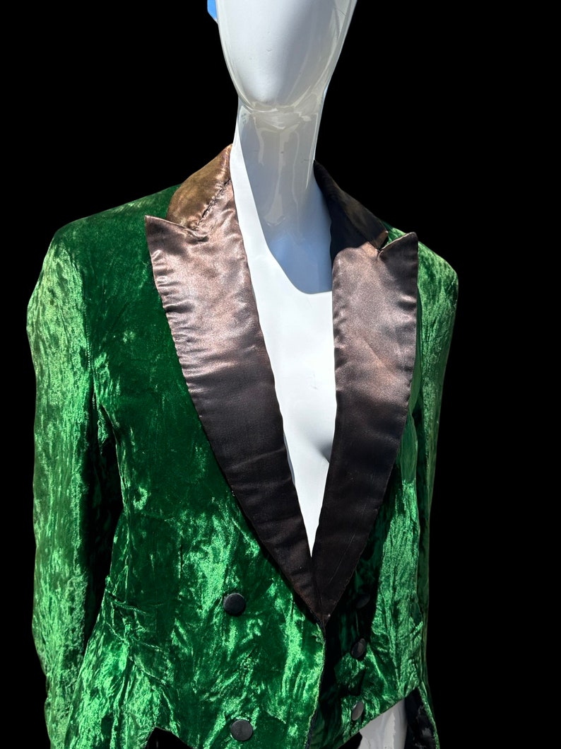 K&ouml;nnte beinhalten: Ein gr&uuml;ner Samtblazer mit schwarzem Satinrevers. Der Blazer hat einen zweireihigen Verschluss und einen langen, spitzen Schwanz.
