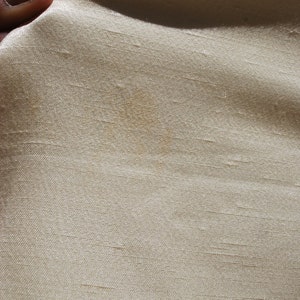 Op de afbeelding: Een close-up van een lichtbeige stof met een kleine bruine vlek.