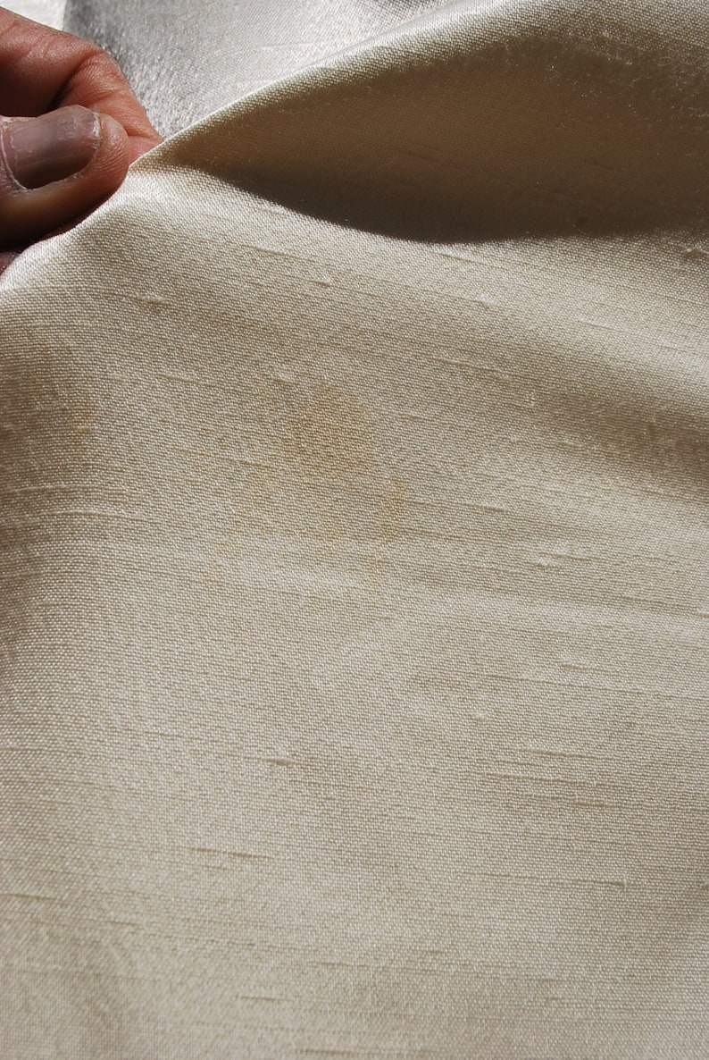 Op de afbeelding: Een close-up van een lichtbeige stof met een kleine bruine vlek.