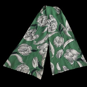 May include: Green fabric with a white and black floral pattern. The fabric is folded in half and the pattern is visible on both sides.