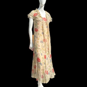 May include: A vintage floral print dress with a sheer overlay and a ruffled neckline. The dress is cream-coloured with red, pink, blue, and yellow flowers.