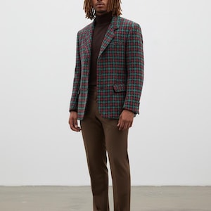 May include: A man wearing a brown turtleneck, brown pants, and black shoes. He is wearing a plaid blazer with red, green, and blue colors. The blazer has two front pockets.