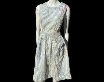 May include: A vintage blue and white striped pinafore dress with red and white trim on the straps. The dress has a single pocket on the front.