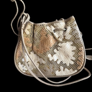 May include: A small, beige drawstring bag made of snakeskin and mesh. The bag has a long strap and is perfect for carrying essentials.