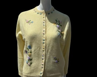 May include: A pale yellow cardigan sweater with floral embroidery. The sweater features a button-up front and long sleeves. Delicate embroidered flowers in shades of pink, blue, and yellow adorn the front and sleeves, adding a touch of vintage charm.