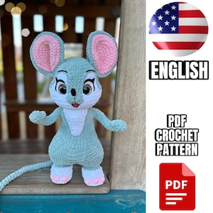 Puede incluir: Un juguete de peluche de ratón tejido a crochet en azul claro y blanco con orejas rosas. El ratón está de pie sobre una superficie de madera. La imagen incluye el texto "ENGLISH" y "PDF CROCHET PATTERN".