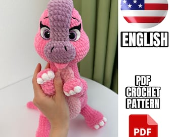 May include: Crochet pattern for a pink dinosaur amigurumi toy. The pattern is available in PDF format and is written in English. The image shows the finished toy and a hand holding it.