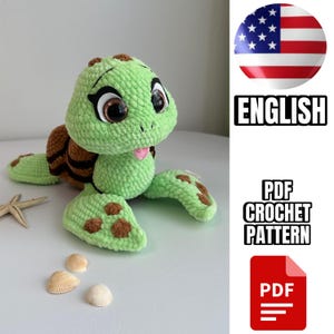 Puede incluir: Un juguete de amigurumi de tortuga verde tejido a crochet con detalles marrones. La tortuga tiene grandes ojos negros y una lengua rosa que sobresale. El juguete está sobre una superficie blanca con conchas.