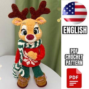 Könnte beinhalten: Eine handgefertigte Häkelpuppe eines Rentiers mit rotem Pullover, grüner Hose und braunen Schuhen. Das Rentier hat braune Geweihe, einen weiß-grünen Schal und eine rote Nase. Der Text "ENGLISH" und "PDF CROCHET PATTERN" ist enthalten.