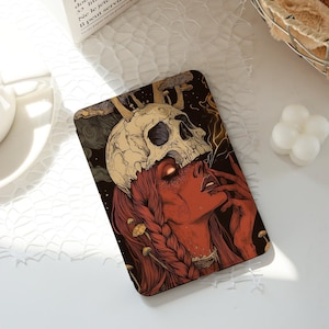 May include: A rectangular art print featuring a woman with red skin and hair, wearing a skull headdress. The artwork has a dark, gothic theme with mushroom and lightning bolt details. The color palette includes red, black, and cream.