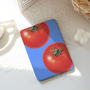 Könnte beinhalten: Eine blaue Handyhülle mit zwei großen, roten Tomaten mit grünen Stielen. Die Tomaten haben Wassertropfen auf einem hellblauen Hintergrund. Die Hülle ist wahrscheinlich aus einem strapazierfähigen Material.