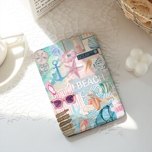 Może przedstawiać: Prostokątne etui na tablet z kolażem ilustracji o tematyce plażowej, zawierające różową rozgwiazdę, niebieską kotwicę, różowe okulary przeciwsłoneczne, klapki, latarnię morską oraz znak z napisem BEACH i OCEAN BLVD w pastelowej kolorystyce.