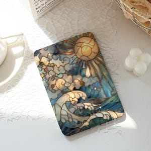 Puede incluir: Un objeto decorativo rectangular con un diseño de vidriera que representa un sol, nubes y olas del océano. La obra de arte utiliza tonos de azul, dorado y blanco, con una apariencia detallada, similar a un mosaico. El sol es un elemento central prominente.