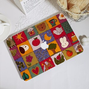 Op de afbeelding: Een kleurrijke laptophoes met een patchwork ontwerp. De hoes bevat illustraties van een beer, appel, maan, konijn en andere grillige elementen. Het Apple-logo is prominent in het midden te zien.