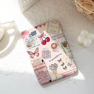Puede incluir: Funda de teléfono decorativa con fondo rosa claro, adornada con pegatinas de libros, mariposas, cerezas y café. El texto incluye "Book Lover", "So Many Books, So Little Time" y "Crying Over Fictional Characters."