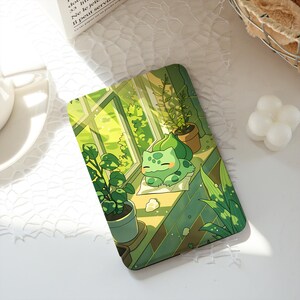 Puede incluir: Funda de teléfono rectangular con una ilustración de dibujos animados de Bulbasaur descansando en un alféizar. El diseño incluye plantas en macetas, una ventana y una paleta de colores verdes. La funda tiene un acabado brillante.