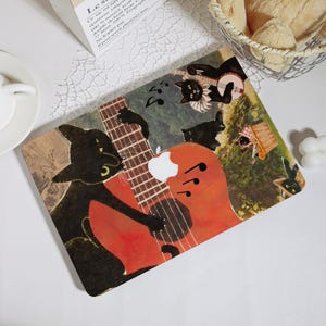 Könnte beinhalten: Eine rechteckige Laptop-Hülle mit einer skurrilen Illustration von schwarzen Katzen, die Musikinstrumente spielen. Das Design umfasst eine Gitarre, ein Banjo und Noten, vor dem Hintergrund einer Picknick-Szene. Die Hülle hat eine warme Farbpalette mit einem weißen Apple-Logo.