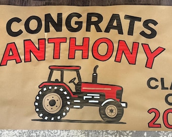 May include: A brown banner with the words "CONGRATS ANTHONY" in black and red lettering. A red tractor illustration is below the name, with the words "CLASS OF 2025" in black and red. The banner is likely for a graduation.