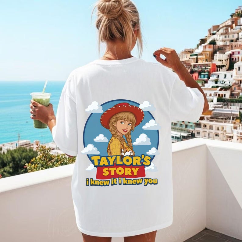 K&ouml;nnte beinhalten: Ein wei&szlig;es T-Shirt mit einem Grafikdruck auf der R&uuml;ckseite. Das Design zeigt eine Zeichentrickfigur mit blonden Z&ouml;pfen und rotem Hut vor einem blauen kreisf&ouml;rmigen Hintergrund mit wei&szlig;en Wolken. Der Text lautet Taylor's Story und I knew it I knew you.