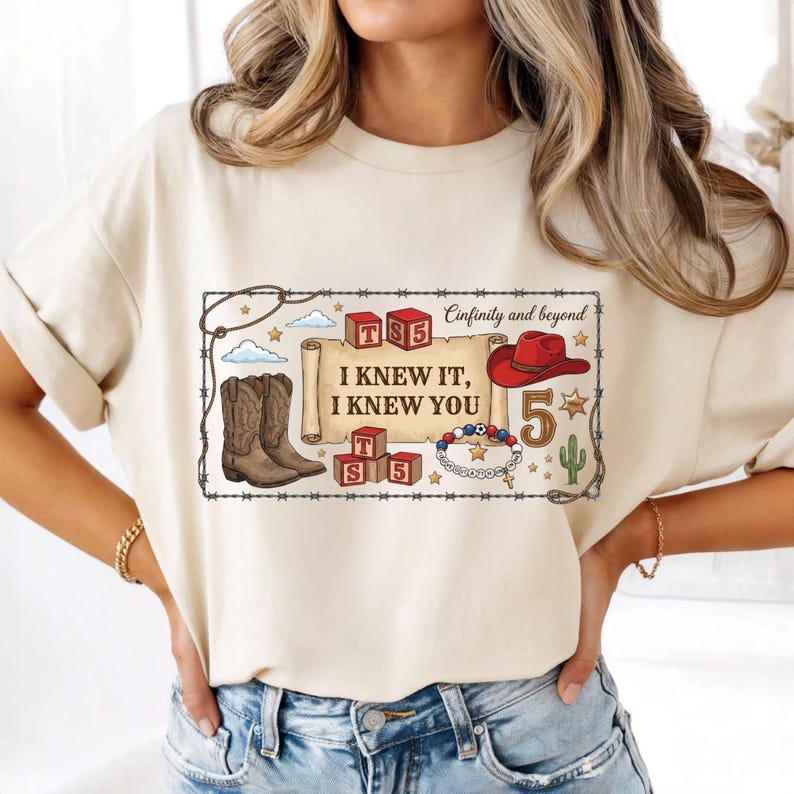 以下が含まれることがあります： クリーム色のTシャツで、『I KNEW IT, I KNEW YOU』という文字が書かれた巻物のグラフィックプリントが施されています。周囲にはカウボーイブーツ、赤いカウボーイハット、『TS5』と書かれたアルファベットブロック、ビーズのブレスレット、サボテンのイラストが描かれています。