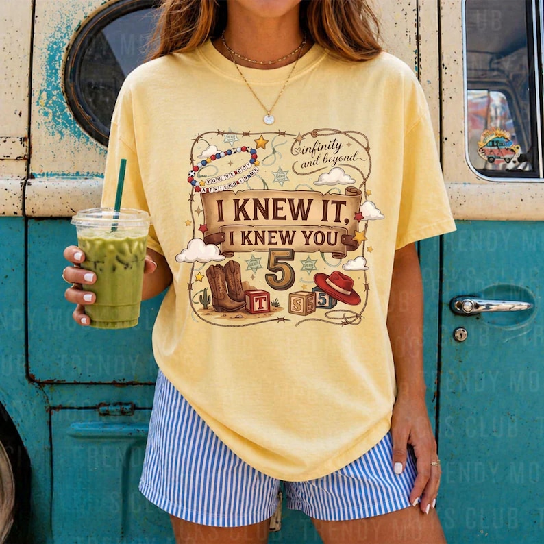 May include: A pale yellow short-sleeve t-shirt featuring a graphic print with the text "I KNEW IT, I KNEW YOU 5" and "infinity and beyond". The design includes illustrations of cowboy boots, a red hat, and blocks with the number 5.