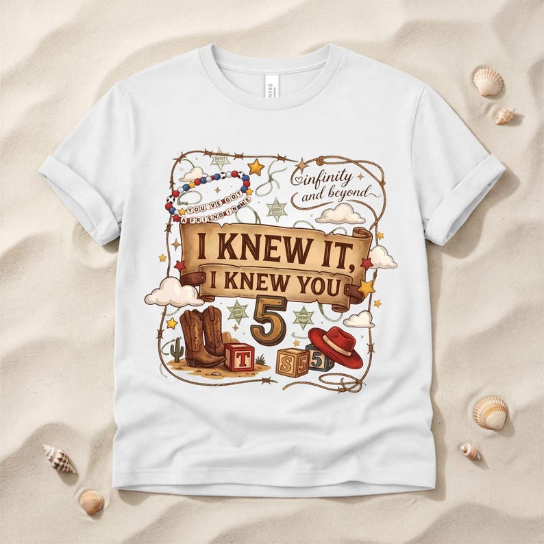 May include: A white short-sleeve t-shirt featuring a graphic print with a lasso border, a beaded bracelet, clouds, stars, and a scroll banner with the text I KNEW IT, I KNEW YOU. Below the banner is the number 5, cowboy boots, blocks, and a red hat.