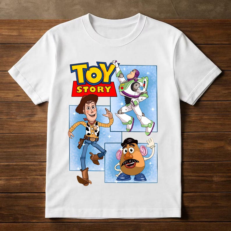 K&ouml;nnte beinhalten: Ein wei&szlig;es Kurzarm-T-Shirt mit einem Grafikdruck des Toy Story-Logos in gelber und roter Schrift. Unter dem Logo befinden sich Illustrationen von Woody, Buzz Lightyear und Mr. Potato Head vor einem hellblauen Hintergrund mit wei&szlig;en Sternen.