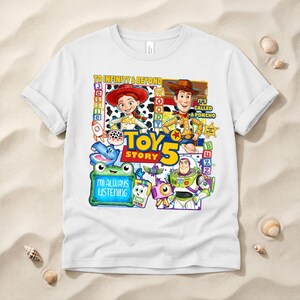 May include: A white short-sleeved t-shirt featuring a colorful graphic print of Toy Story characters including Jessie, Woody, and Buzz Lightyear. The design includes the text TO INFINITY & BEYOND, TOY STORY 5, IT'S CALLED A PONCHO, and I'M ALWAYS LISTENING.