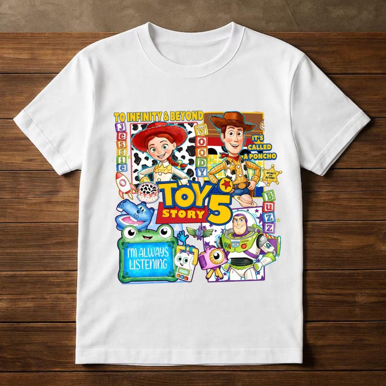 May include: A white short-sleeved t-shirt featuring a colorful Toy Story 5 graphic print. The design includes characters Jessie, Woody, and Buzz Lightyear, along with text that reads To Infinity & Beyond, It's Called A Poncho, and I'm Always Listening.