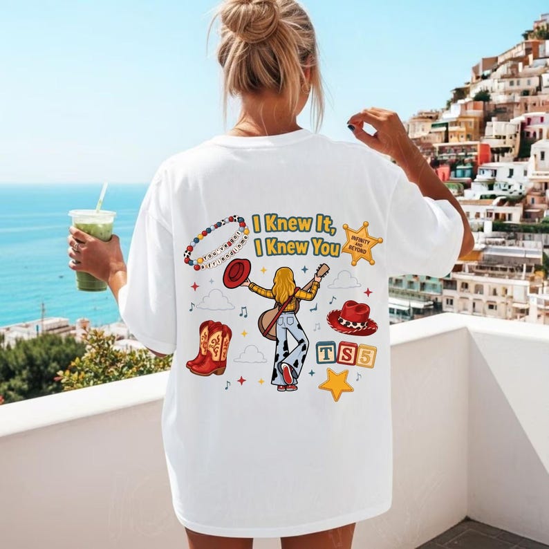 K&ouml;nnte beinhalten: Ein wei&szlig;es T-Shirt mit einem Grafikdruck auf der R&uuml;ckseite und dem Text I Knew It, I Knew You. Das Design zeigt ein Perlenarmband, einen roten Cowboyhut, einen roten Cowboystiefel, eine gitarrespielende Figur, einen Stern und TS5-Bl&ouml;cke.