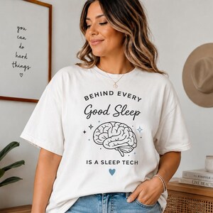 Peut inclure: Un t-shirt à manches courtes blanc cassé avec le texte noir BEHIND EVERY Good Sleep IS A SLEEP TECH, une illustration centrale d'un cerveau humain, de petites étoiles décoratives et une petite icône de cœur bleu sous le texte.