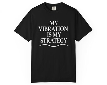 Op de afbeelding: Zwart T-shirt met de witte tekst "MY VIBRATION IS MY STRATEGY". De tekst is vetgedrukt en zonder schreef, gecentreerd boven een gebogen lijn. Het T-shirt heeft korte mouwen en een ronde hals.