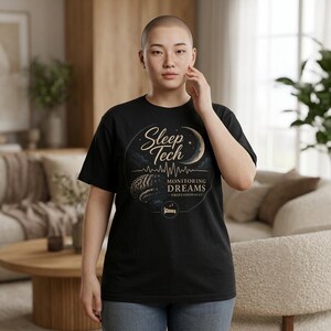 Peut inclure: T-shirt noir avec un motif circulaire. Le motif comprend le texte "Sleep Tech" et "Monitoring Dreams Professionally", un croissant de lune, une illustration de cerveau et une ligne de battement de cœur. Le t-shirt est porté par une personne.