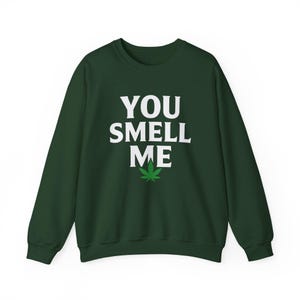 Puede incluir: Sudadera verde oscuro con el texto blanco "YOU SMELL ME" y un gráfico de hoja de cannabis verde. La sudadera tiene cuello redondo y mangas largas.