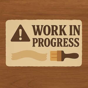 Puede incluir: Un letrero rectangular con las palabras "WORK IN PROGRESS" en letras marrones oscuras. El letrero también presenta un símbolo de signo de exclamación marrón, una cinta de pintura beige y una ilustración de pincel marrón y beige. El fondo es una veta de madera.