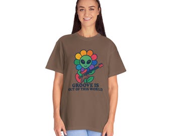 May include: Brown t-shirt featuring a colorful graphic of an alien playing a guitar inside a flower. The flower has rainbow petals and the alien is green. The text "GROOVE IS OUT OF THIS WORLD" is below the graphic.