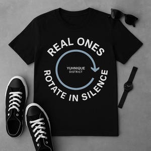 Peut inclure: T-shirt noir avec un texte blanc qui dit "REAL ONES ROTATE IN SILENCE" avec un cercle et une flèche graphique au centre. Le texte "YUHNIQUE DISTRICT" est à l'intérieur du cercle.